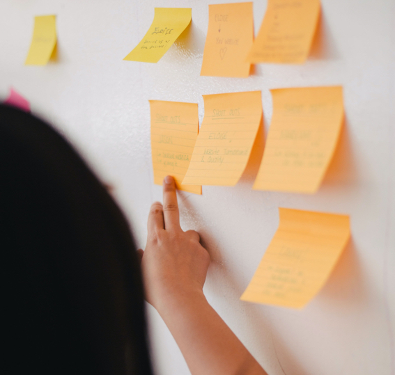 Woman's hand pointing at post it notes on whiteboard during brainstorming session