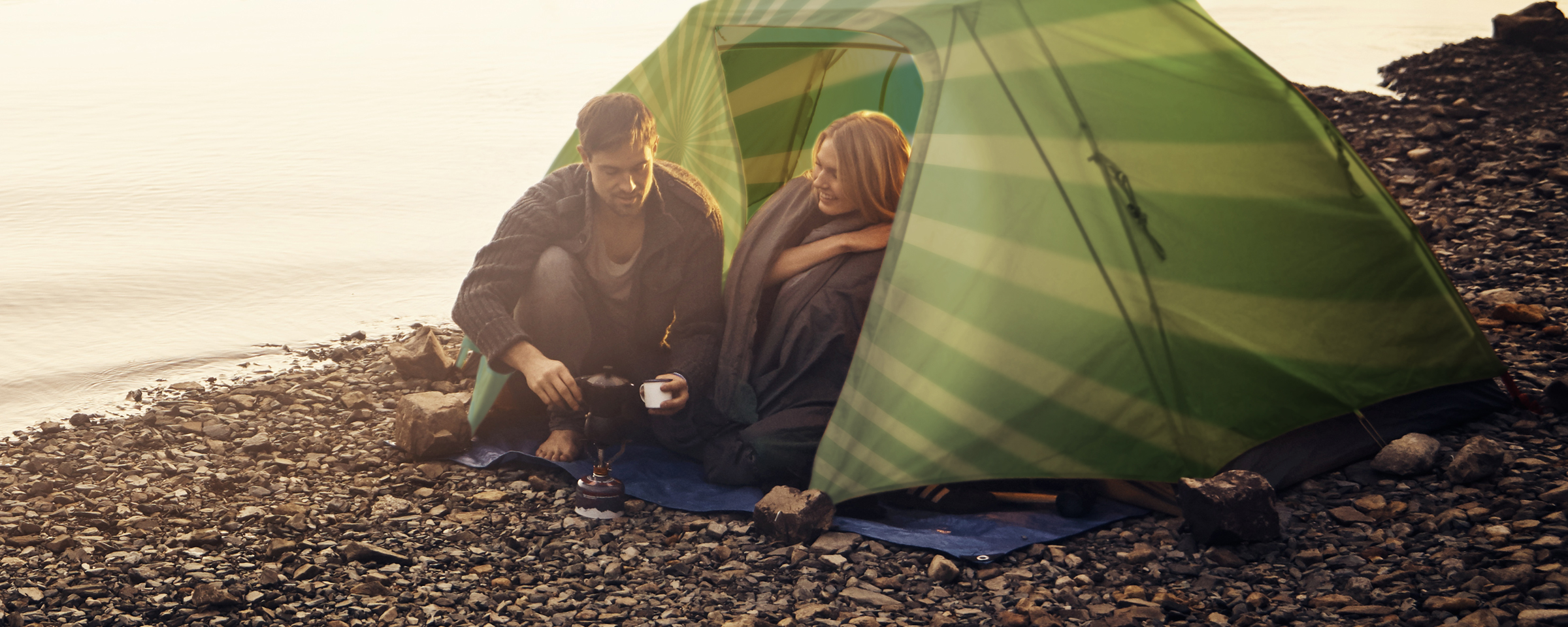 man and women sitting in camping tent by a lake